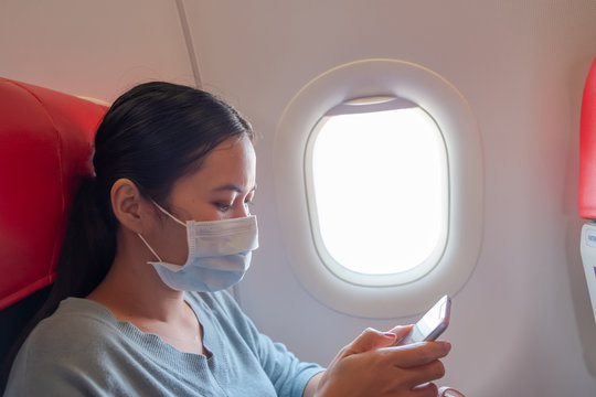 Asian girl use a protection mask for coronavirus or covid 19 in airport. Thai lady playing with her phone on airplane.