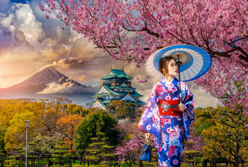 Asian woman wearing japanese traditional kimono at Osaka Castle and full cherry blossom, with Fuji mountain background, Japan.