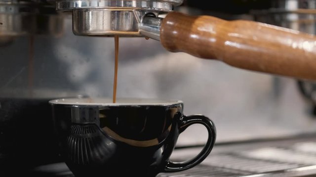 The espresso coffee is being poured from machine into a coffee mug