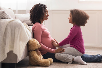 Little afro girl touching her pregnant mom belly, feeling baby kicks