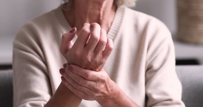 Senior grandmother massaging hand suffering from joint pain. Older woman having rheumatoid arthritis. Elder adult lady touching wrist feeling hurt. Osteoarthritis geriatric disease concept. Close up