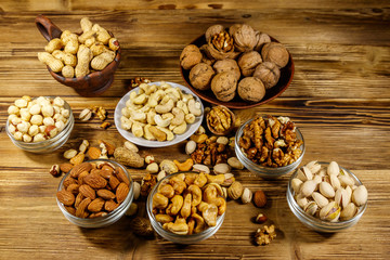 Assortment of nuts on wooden table. Almond, hazelnut, pistachio, peanut, walnut and cashew in small bowls. Healthy eating concept