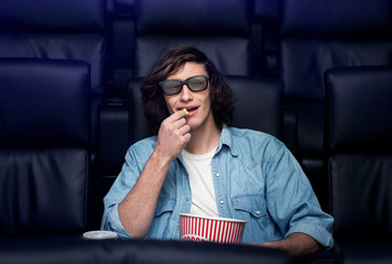 Enjoying alone time in movies. Cheerful young man with 3D glasses and popcorn in empty cinema