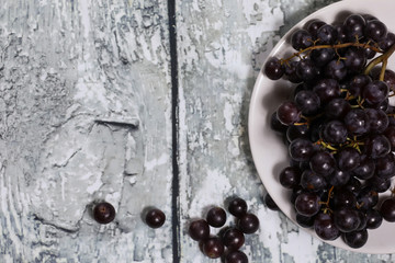 Red grape on a plate on a wooden background.