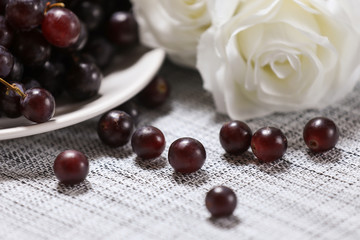 Red grape in a plate with white rose flower on a background.