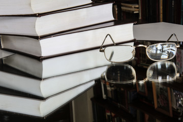 Golden-rimmed glasses lie on the mirror. Near a stack of books. Reflection in the mirror. Library. Concept - vintage, leisure, education