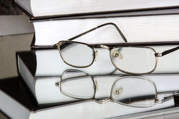 Golden-rimmed glasses lie on the mirror. Near a stack of books. Reflection in the mirror. Library. Concept - vintage, leisure, education