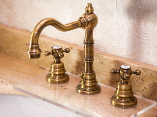 vintage faucet with copper valve taps on a marble stone washbasin, close up.