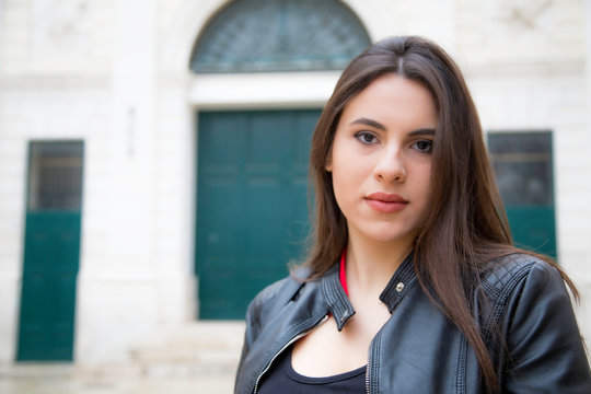 Bellissima donna italiana con un sorriso solare e capelli lunghi castani lisci indossa un top nero una camicia rossa e giacca nera di pelle in esterno 