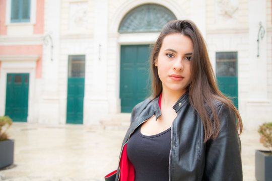 Bellissima donna italiana con un sorriso solare e capelli lunghi castani lisci indossa una camicia rossa e giacca nera di pelle in esterno di una citt&agrave; medievale