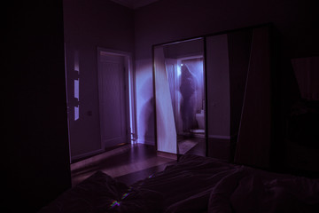 A creepy bedroom scenery, Silhouette of scary person standing reflected in mirror with mist and...
