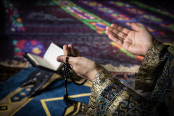 Obraz premium Muslim woman praying for Allah muslim god at room near window. Hands of muslim woman on the carpet praying in traditional wearing clothes, Woman in Hijab, Carpet of Kaaba, Selective focus, toned