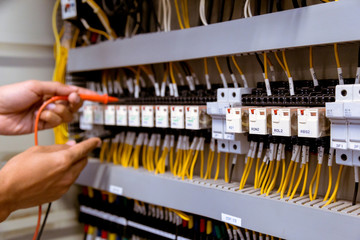 Electrician measurements with multimeter testing current electric in control panel.