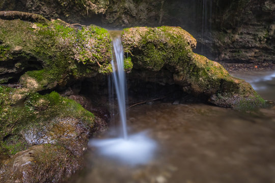 Small waterfall in the forest with a water jet and mossy tree roots. 