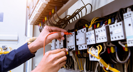 Electrician measurements with multimeter testing current electric in control panel.