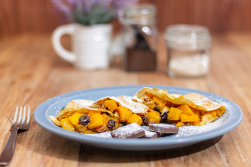 Mango crepes, with 3 chocolate feet, on a blue plate on a wooden table