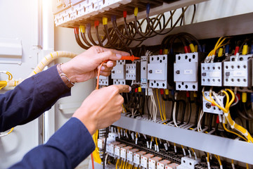 Electrician measurements with multimeter testing current electric in control panel.