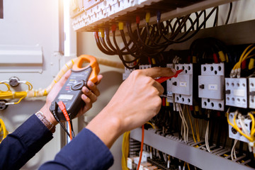 Electrician measurements with multimeter testing current electric in control panel.