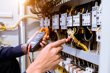 Electrician measurements with multimeter testing current electric in control panel.