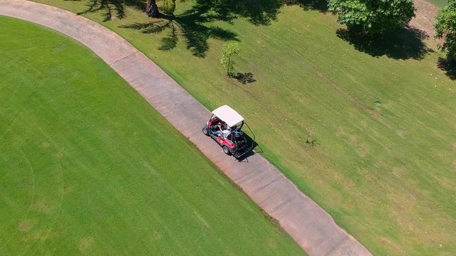 Electric golf cart buggy driving on tropical green golf course, aerial follow view