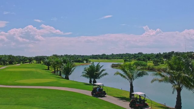 Electric golf carts driving beside lake on tropical green golf course, aerial view
