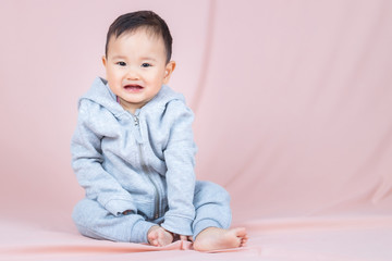 Fototapeta premium Asia baby boy wearing gray shirt and pants, sitting on floor and peach background.