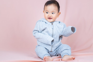 Asia baby boy wearing gray shirt and pants, sitting on floor and peach background.