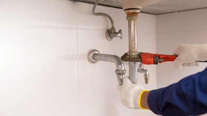 Plumber fixing white sink pipe with adjustable wrench.