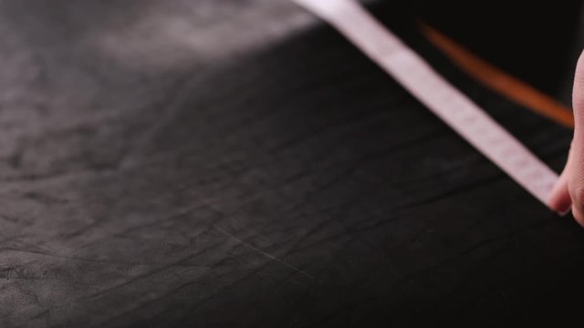 A leather master is measuring material with a tape measure. The tanner is making hand-made leather men&rsquo;s belt.