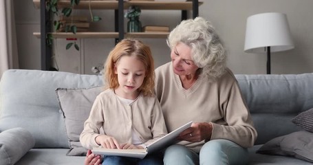 Smart kid girl granddaughter learning reading with old grandma at home. Senior grandmother baby sitter teaching cute small grandkid of 6-7 years enjoying preschool elementary education hobby concept. - Powered by Adobe