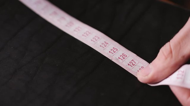 A leather master is measuring material with a tape measure. The tanner is making hand-made leather men&rsquo;s belt.