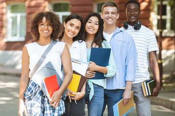 Multiethnic group of students standing near college building, posing at camera