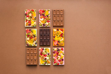 Chocolate of various colors and colored fillings with slices of fruit nuts on a brown background . Top view flat layout.