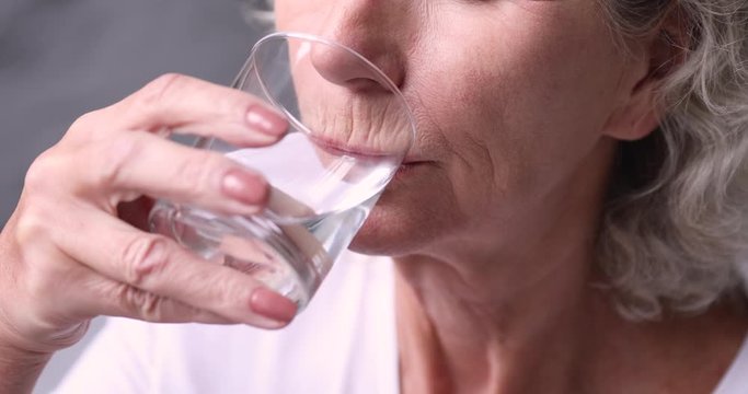 Thirsty healthy senior adult woman holding glass drinking fresh mineral pure water. Dehydrated old lady feels thirst hydrates healthcare balance. Elder person morning hydration concept. Close up view