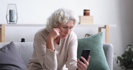 Frustrated senior lady reads bad news in mobile message concept. Sad depressed 70 years old woman looking at smart phone feels shocked. Worried elder female user customer lost money on scam fraud - Powered by Adobe