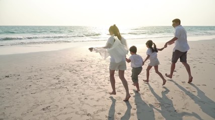 4K Happy Asian family parent and two child walking on the beach and having fun together with smiling at summer sunset. Young Asian family relaxing and enjoying lifestyle in travel holiday vacation.
