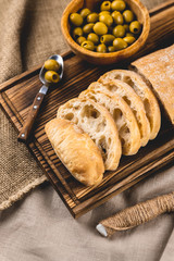 Fresh italian ciabatta sliced on a wooden board with olives and olive oil
