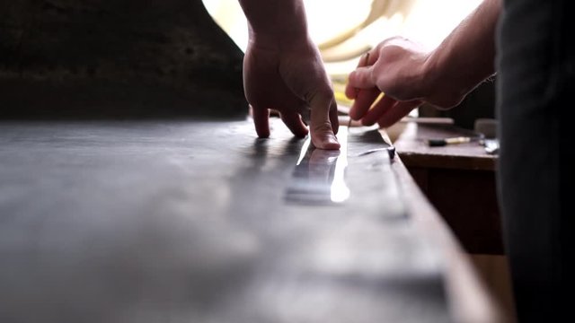 A tanner is cutting black leather sheet with a razor and metre. The master is making a leather belt for men.