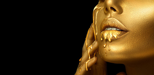 Gold Paint smudges drips from the face lips and hand, lipgloss dripping from sexy lips, golden liquid drops on beautiful model girl's mouth, gold metallic skin make-up. Beauty woman makeup close up.