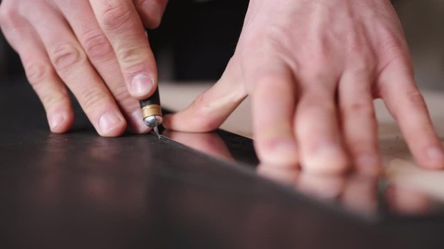 A tanner is cutting black leather sheet with a razor and metre. The master is making a leather belt for men.