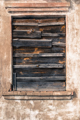 An old window in an abandoned house is clogged with gray boards. Boarded up window frame. Old weathered stucco and whitewash. Vintage photo abandoned