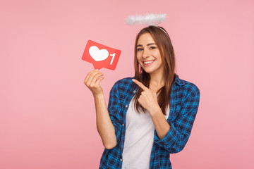 Portrait of happy charming girl with angelic halo smiling and pointing at social media like icon,...