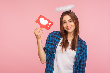 Portrait of positive charming girl with angelic halo smiling and holding social media like icon,...
