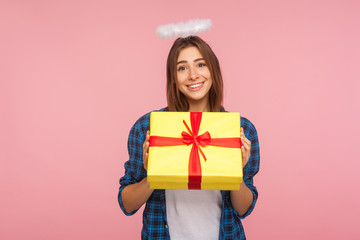 Present from angel. Portrait of generous happy beautiful girl with halo over head holding gift box and smiling kindly, congratulating on birthday. indoor studio shot isolated on pink background