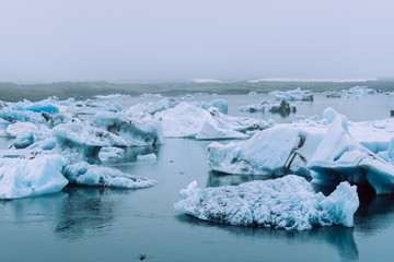 Fototapeta na wymiar Bright white glaciers covered with dense fog in the blue waters of Jokulsalron glacial lake in Iceland