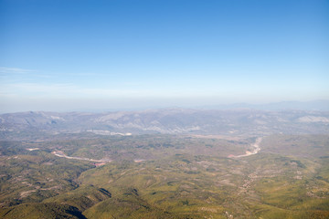 Areal view of a curvy highway road going through the valleys and forest with background mountains and blue sky