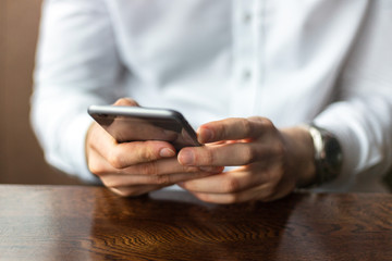 Closeup of hands of young businessman wearing a white fashion shirt with a mobile phone in a cafe...