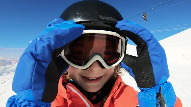 Smiling child skiing and waving hand on snow mountain and blue sky background. Happy boy enjoying winter vacation on ski slopes in sunny day. Having fun with outdoors activity, sport