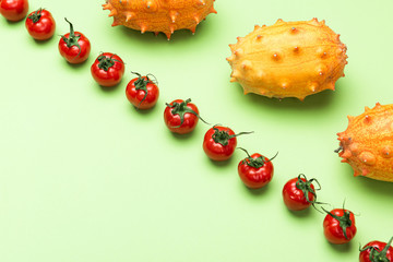 Red Tomatoes and Yellow Kiwano Flat Lay Pattern. Green Background with Raw Vegetables