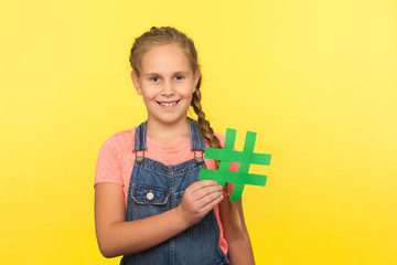 Internet trends, viral web content. Portrait of cheerful little girl with braid in denim overalls...